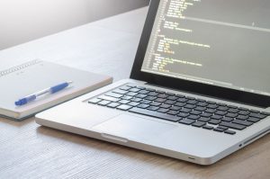 Laptop with a code editor open next to a notebook and pen on a wooden desk, representing WordPress website editing