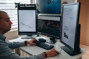 Professional working across three computer monitors showing multiple dashboards