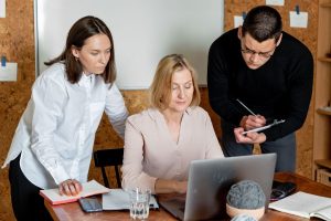 Colleagues gathered around a laptop in a business meeting while one person takes notes